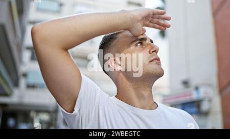 A handsome young hispanic man shielding eyes from sun on a city street. Stock Photo