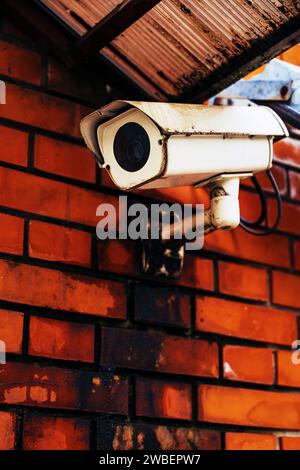 Old worn surveillance camera equipment mounted on red brick wall, selective focus Stock Photo