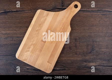 Empty wooden cutting board and curved handle on wooden background. Copy space. Stock Photo
