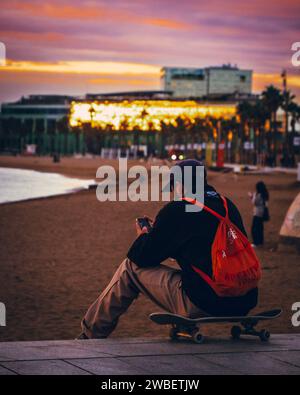 Guy sitting on skateboard by the sea side taking picture Stock Photo