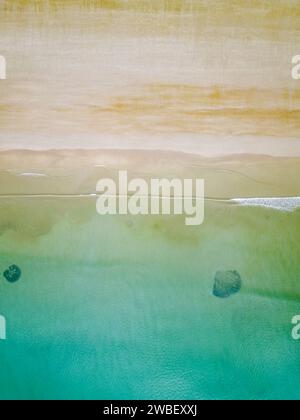 Top down area view of waves lapping on the shore of a large, empty tropical beach Stock Photo