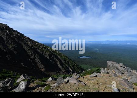 This image depicts a majestic mountain range in the background, with clouds in the sky and the sun shining brightly Stock Photo