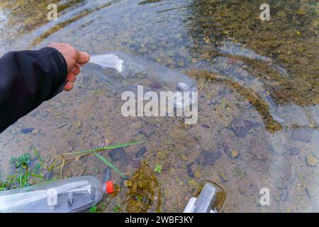 Man collecting plastic bottles on the shore of a river, environmental and ecological concept Stock Photo