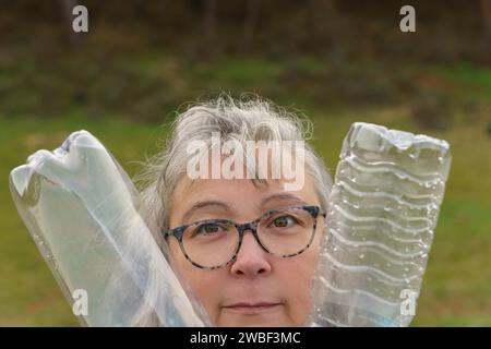 Close-up of an older white-haired woman with glasses holding two empty plastic bottles collected in the field, concept of ecology and care for the Stock Photo