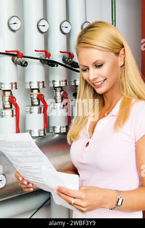 A young blonde housewife checks the heating system in the basement, utility bill, energy consumption, heating bill Stock Photo