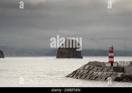 Breakwater and lighthouse by the sea with a rocky island 'Iieu em Pe' in the background on a foggy day, Iieu Deitado, Iieu em Pe, Horta, Faial Stock Photo