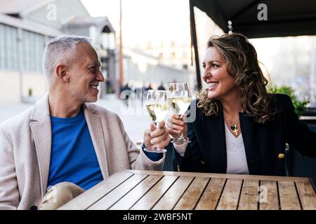 Lovely mid adult couple toasting with wine while sitting in a terrace restaurant. Romantic date of a middle age woman and man drinking with glasses at Stock Photo
