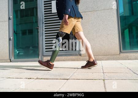 Lower part of an unrecognizable businessman with prosthetic leg walking along a financial district street Stock Photo