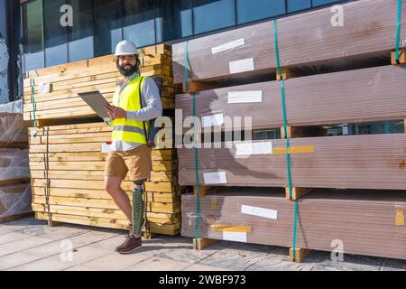 Engineer with prosthetic leg working outdoors with paperwork in a construction site leaning on a wall Stock Photo