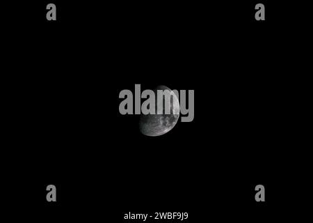 A half-moon illuminated against a backdrop of inky dark clouds Stock Photo