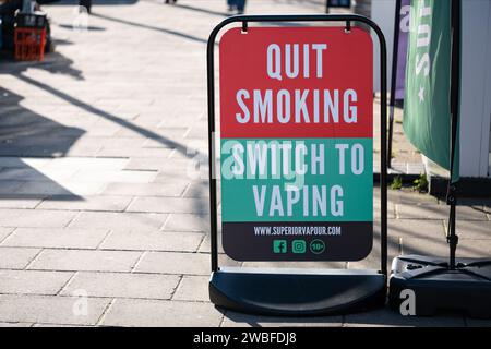 A large street sign advising people to quit smoking and switch to vaping. The sign is place on a city street pavement outside of a vaping shop Stock Photo