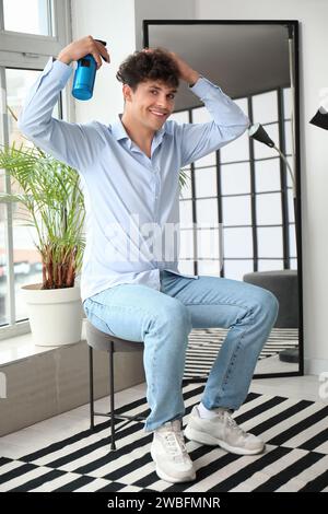 Handsome young man applying hair spray on his curly hair in hallway Stock Photo