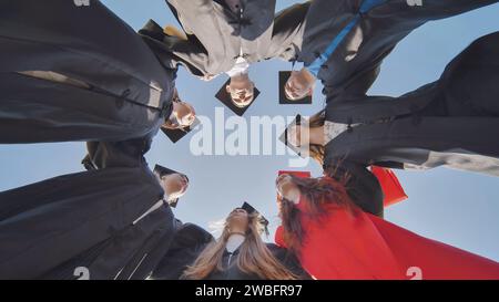 College graduates in a circle stand hugging each other. Stock Photo