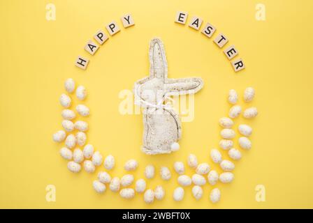 Handmade Easter decor, stylish Easter eggs, textile rabbit on yellow background. Easter wreath shape Stock Photo