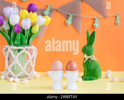 Two natural colored Easter eggs on background of spring flowers and an Easter bunny. The concept of eco, colors and decor. Stock Photo
