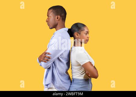 Black couple standing back-to-back, arms crossed, on yellow background Stock Photo