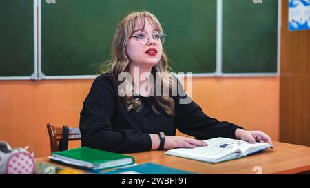 A schoolgirl in the role of a teacher sits at her desk. Stock Photo