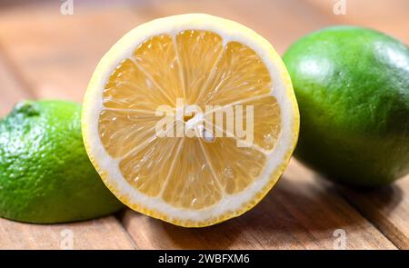 Half Cut Fresh Lemon with green limes on either side, on a wooden cutting board. Stock Photo