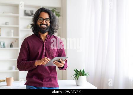 Handsome Indian Man With Digital Tablet Standing Near Desk At Home Stock Photo