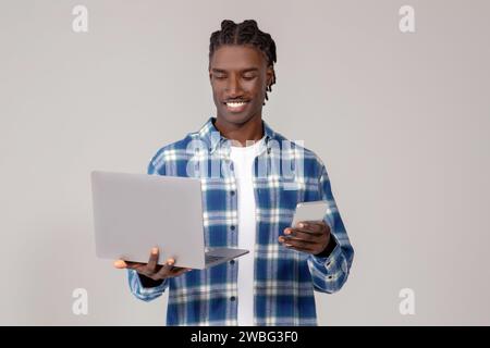 Focused young black man using laptop and holding smartphone Stock Photo