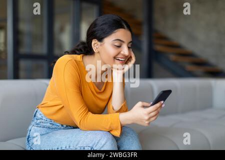 Happy young indian woman using her smartphone in living room at home Stock Photo