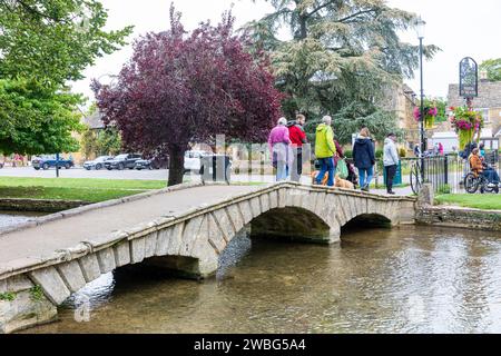 Cotswolds England , people with dogs walk across one of the low stone bridges in Bourton on the Water village, crossing the River Windrush, England,UK Stock Photo