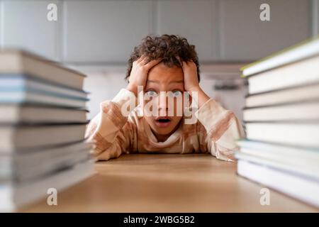 Stressed black boy surrounded by towering stacks of books Stock Photo