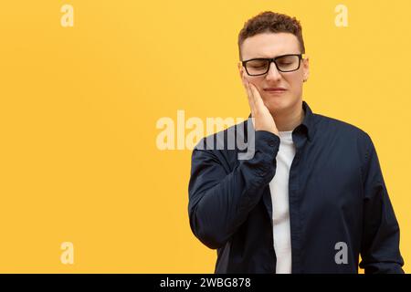 Unhappy young european guy holding hand on cheek Stock Photo