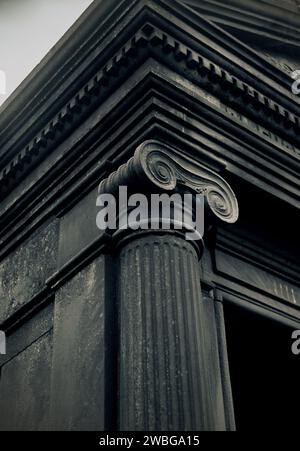 A column of dark stone supports the roof of the old building. Classical architecture and travel. Dark and gloomy. Stock Photo