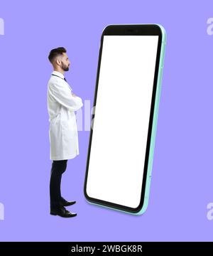 Man in white coat standing in front of big smartphone on lilac background Stock Photo