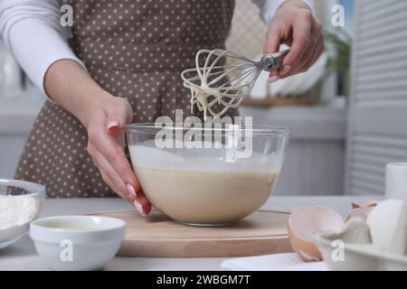 Woman making dough with whisk in bowl at table, closeup Stock Photo