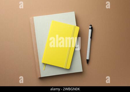 Different notebooks and pen on light brown background, top view Stock Photo