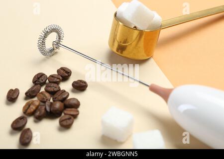 Milk frother wand, coffee beans and sugar cubes on color background, closeup Stock Photo