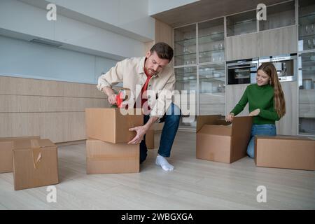 Pleased marrieds packing cardboard boxes to move in new home together. Family prepare to relocate. Stock Photo