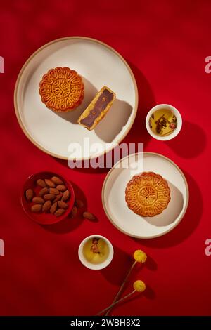 White cups filled with tea and dried flowers arranged with tasty mooncakes and a red dish of almond nuts. Round moon cakes with beautiful patterns are Stock Photo
