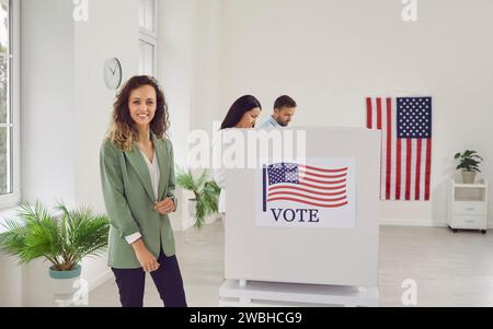 Voter woman looking at camera standing at vote center near voting booth on election day. Stock Photo