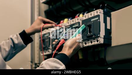 Electrician engineer work tester measuring voltage and current of power electric line in electical cabinet control. Stock Photo