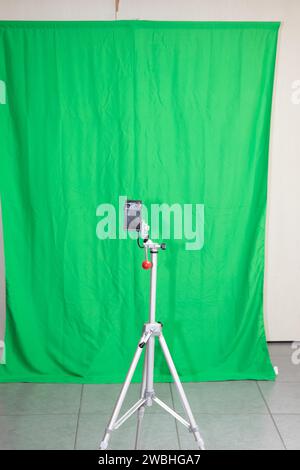 Chromakey green fabric background for photographer or cameraman studio and tripod with camera for shooting Stock Photo