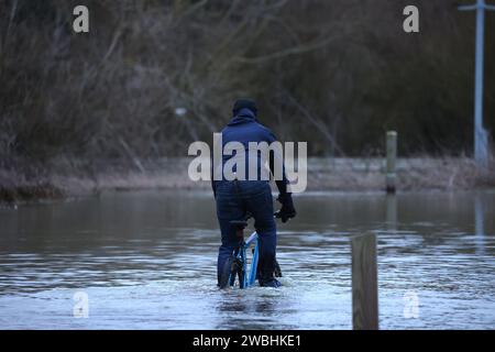 A cylist rides through deep water as flooding is still a problem in Peterborough after the River Nene breached its banks at Orton Mere in Peterborough, Cambridgeshire, on 8th January 2024. Stock Photo