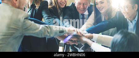 Diverse business team joins hands together in a show of unity and collaboration at a bright office. Stock Photo