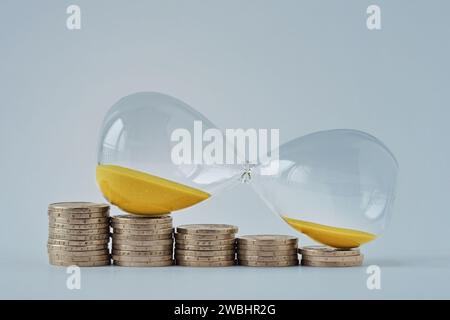 Hourglass on decreasing piles of coins - Concept of money and time Stock Photo