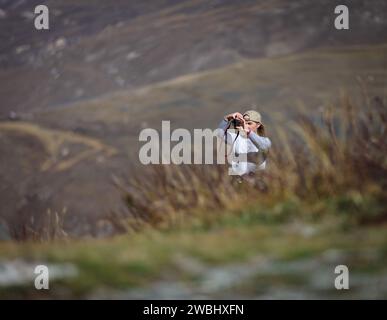 Young woman shooting delightful scenery uphill Stock Photo