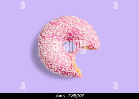 One bitten pink donut with white sprinkles on a purple background. Fresh donut poured with pink glaze. Stock Photo
