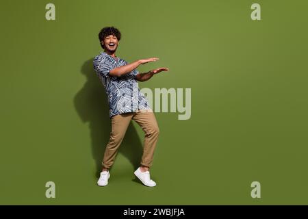 Full body photo of crazy hispanic guy wearing trendy apparel doing dynamic moves catch rhythm dancing isolated on khaki color background Stock Photo