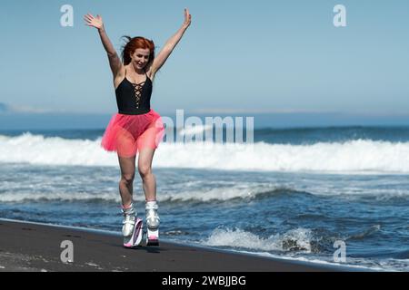 Happy sportswoman in Kangoo Jumps boots, black one-piece swimsuit and short skirt jumping and running on black sand Stock Photo
