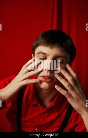 close up photo, pensive young man in shirt and suspenders touching his face on red background Stock Photo