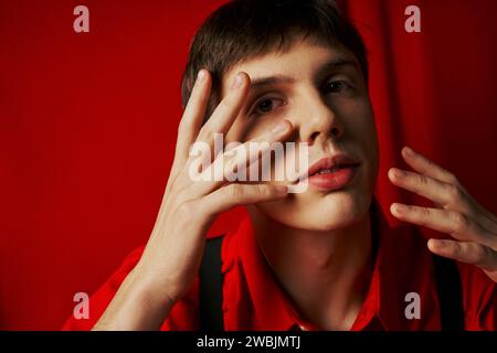 close up shot, pensive young man in shirt and suspenders touching his face on red background Stock Photo