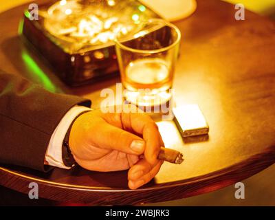 Glass of whiskey with smoking cigar and ice cubes on wooden table Stock Photo