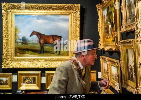 London, UK. 11th Jan, 2024. A collector examines oil paintings in Cambridge Fine Arts - The Mayfair Antiques & Fine Art Fair, London Marriott Hotel Grosvenor Square. Credit: Guy Bell/Alamy Live News Stock Photo