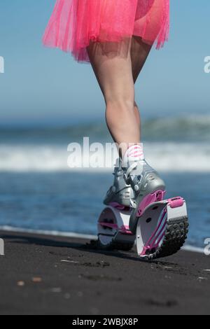 KAMCHATKA, RUSSIA - JUNE 15, 2022: Rear view of female athlete legs in sports Kangoo Jumps boots, running on sandy beach during summer outdoors fitnes Stock Photo